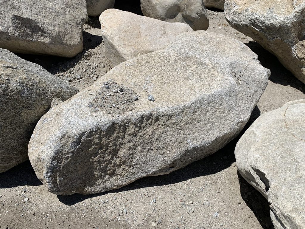 Large rocks sitting on sandy ground under sunlight.