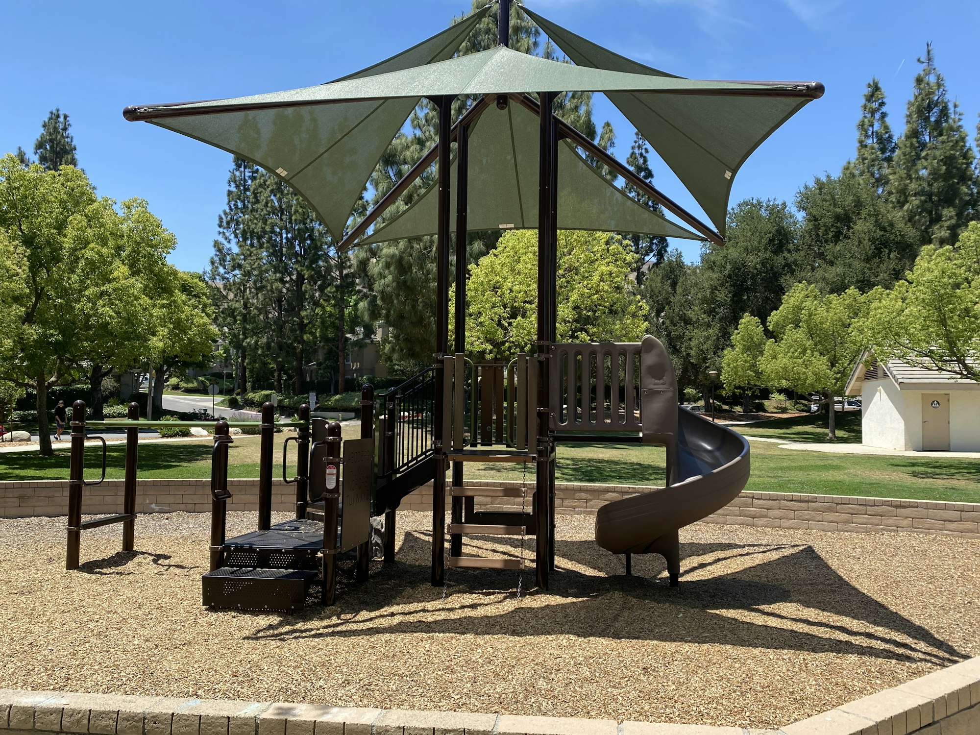 Playground with slides and a canopy, surrounded by trees and grass.
