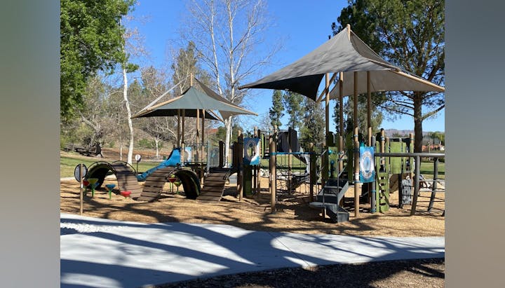 Playground with slides, climbing structures, and shade canopies, surrounded by trees.
