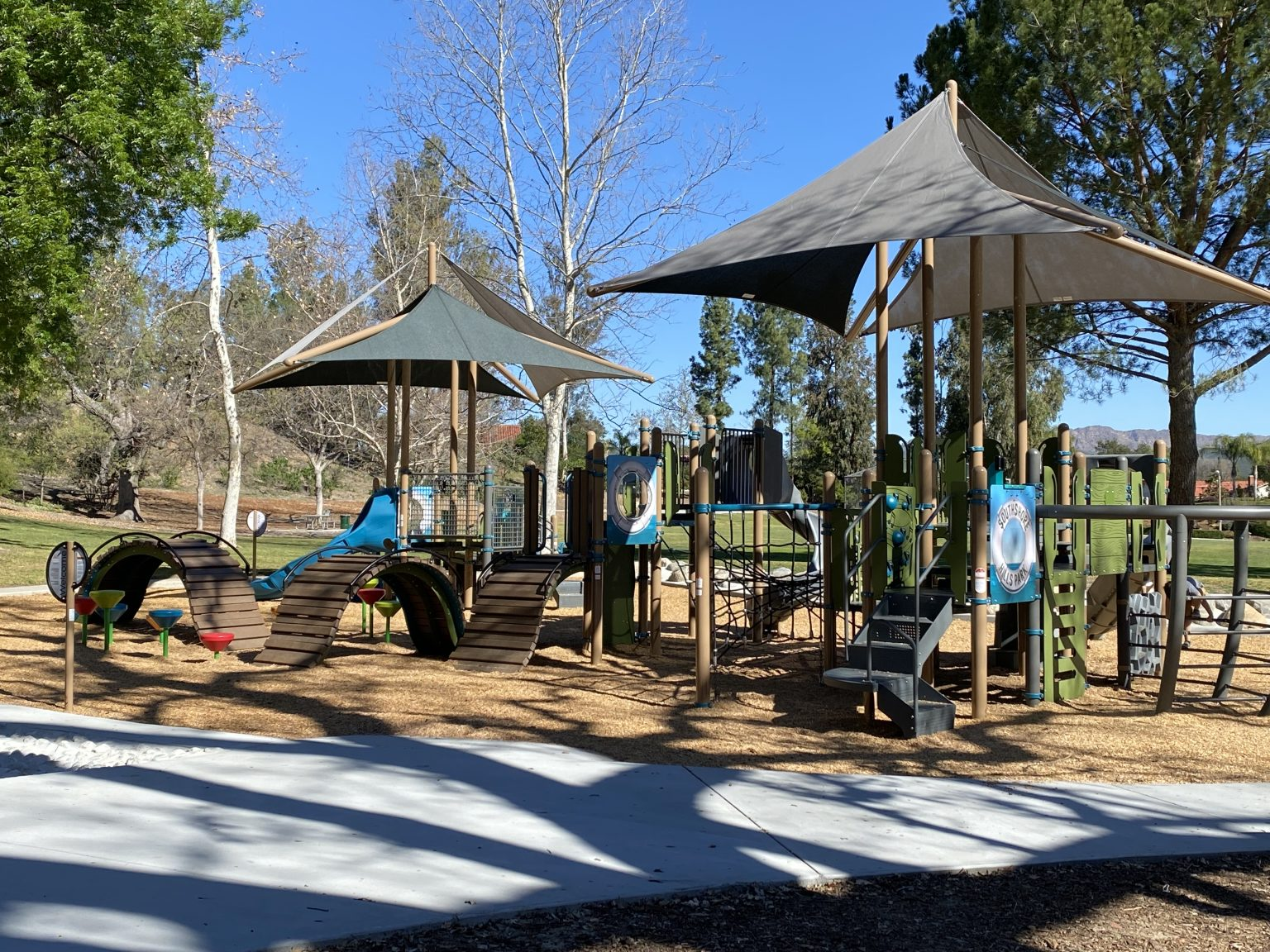 Playground with slides, climbing structures, and shade canopies, surrounded by trees.