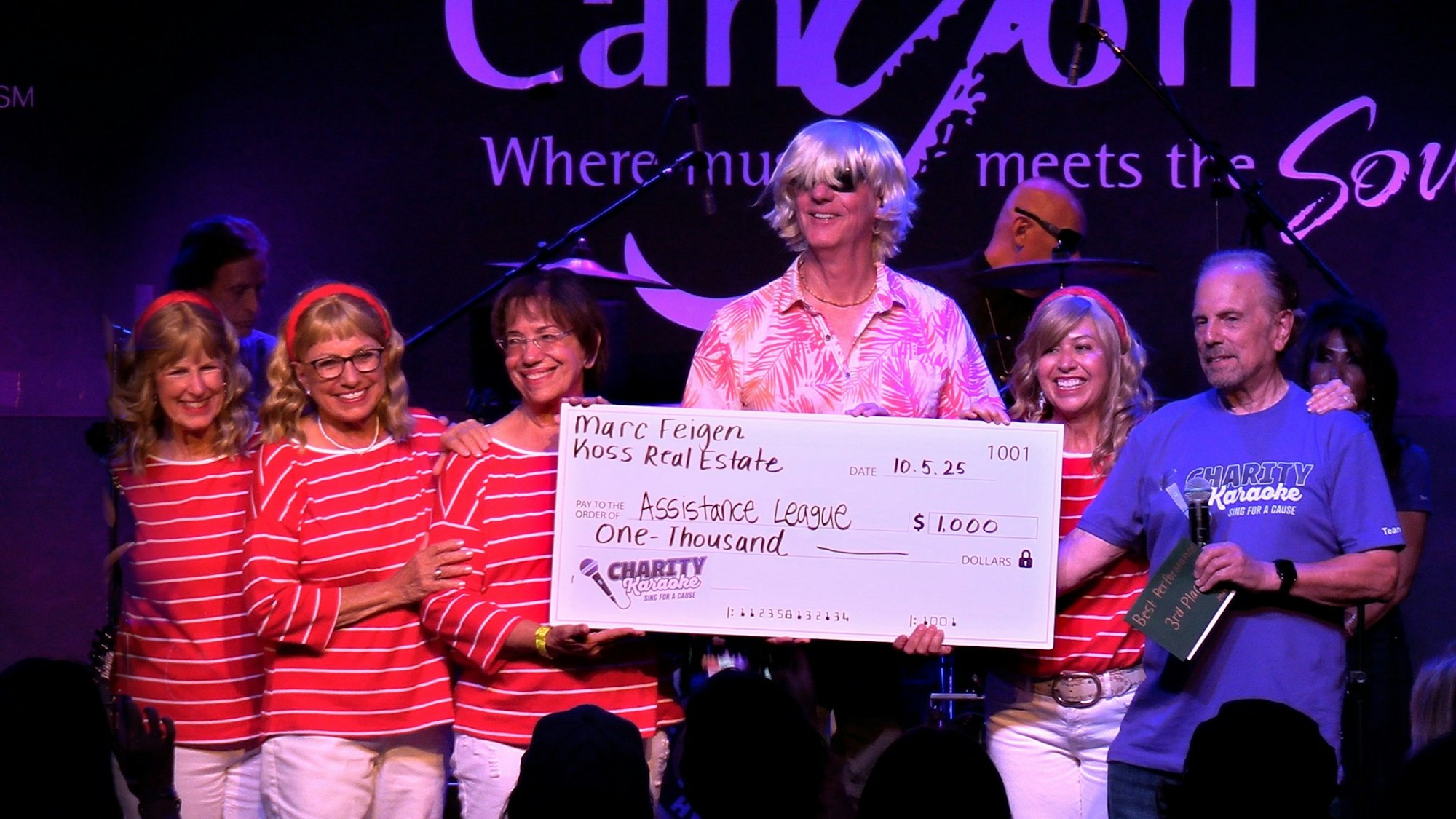 A group of people on stage holding a large check for $1,000, likely from a charity event.