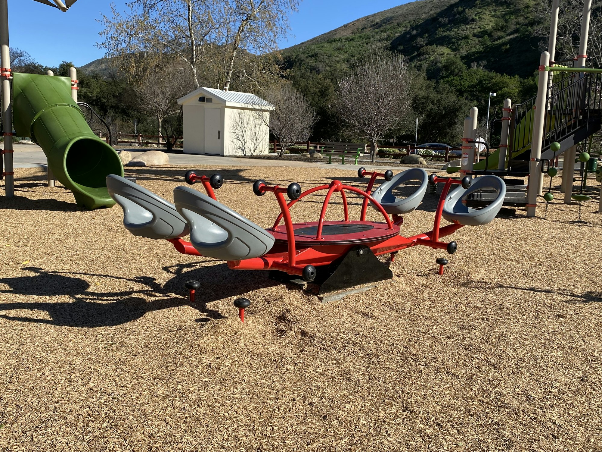 Playground with a unique spinning ride, slides, climbing structures, and woodchip ground cover.