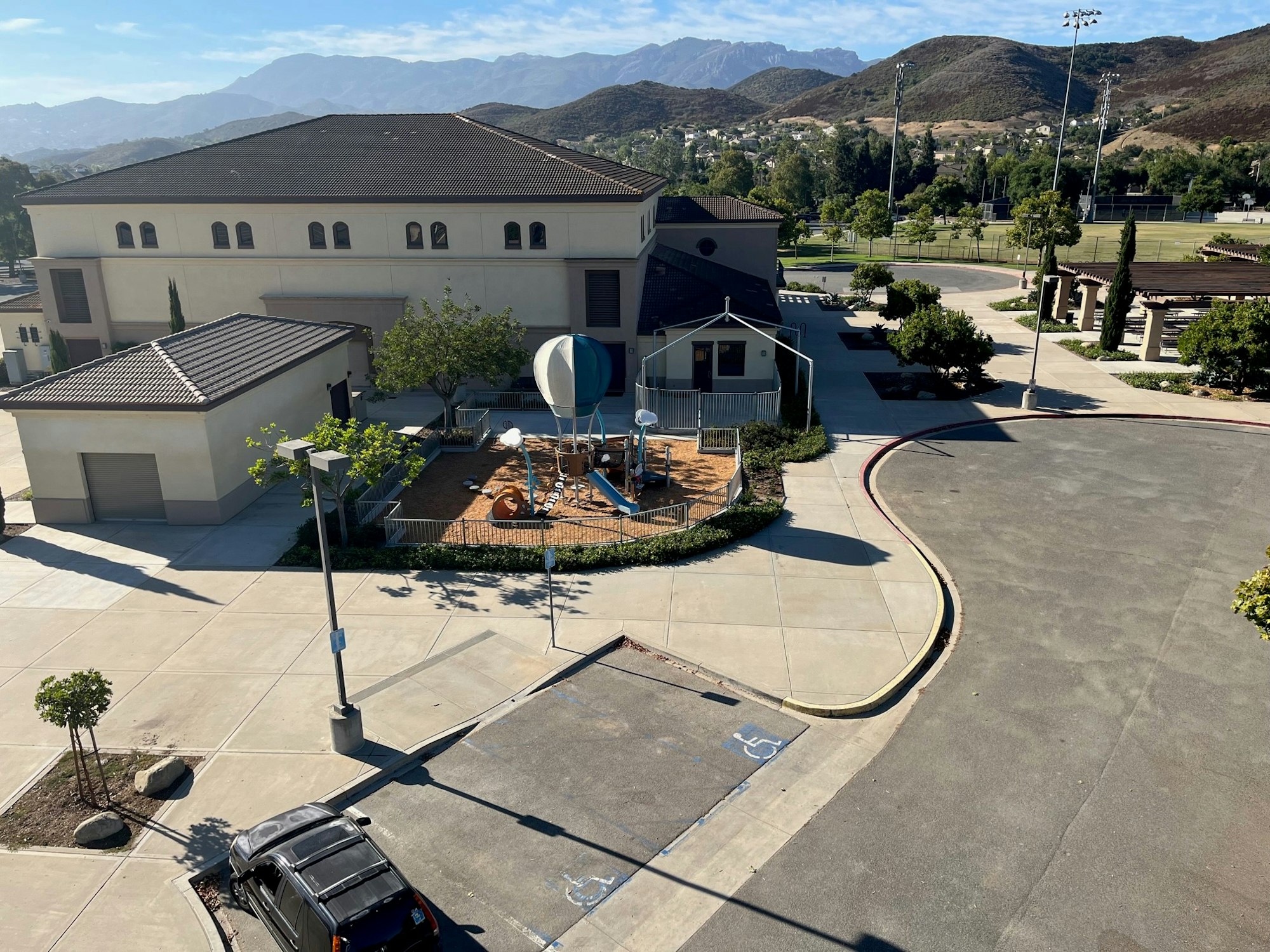 A playground with a hot air balloon structure, building, and parking lot surrounded by mountains under a blue sky.