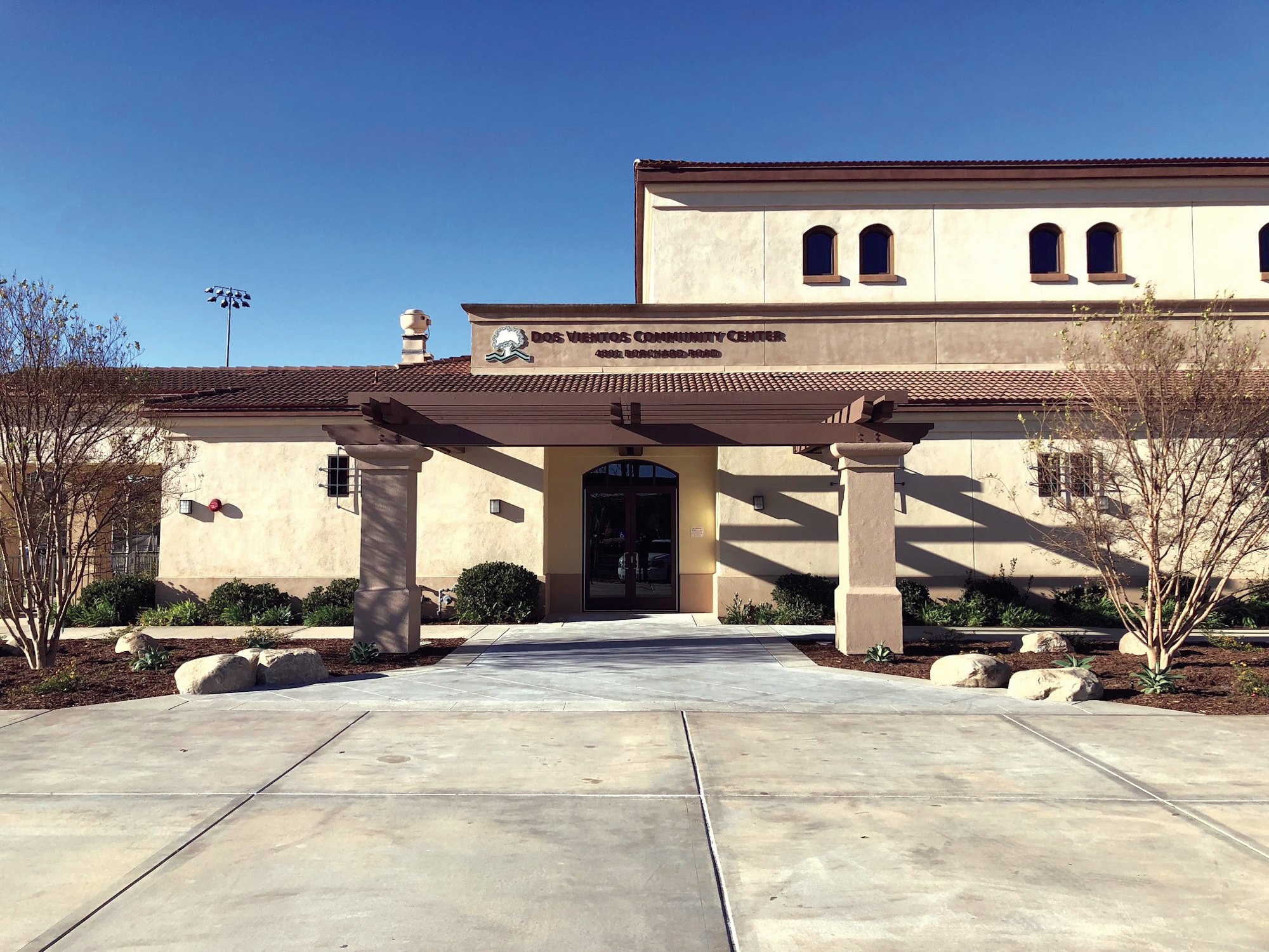 Dos Vientos Community Center building with a pathway and landscaping under a clear blue sky.