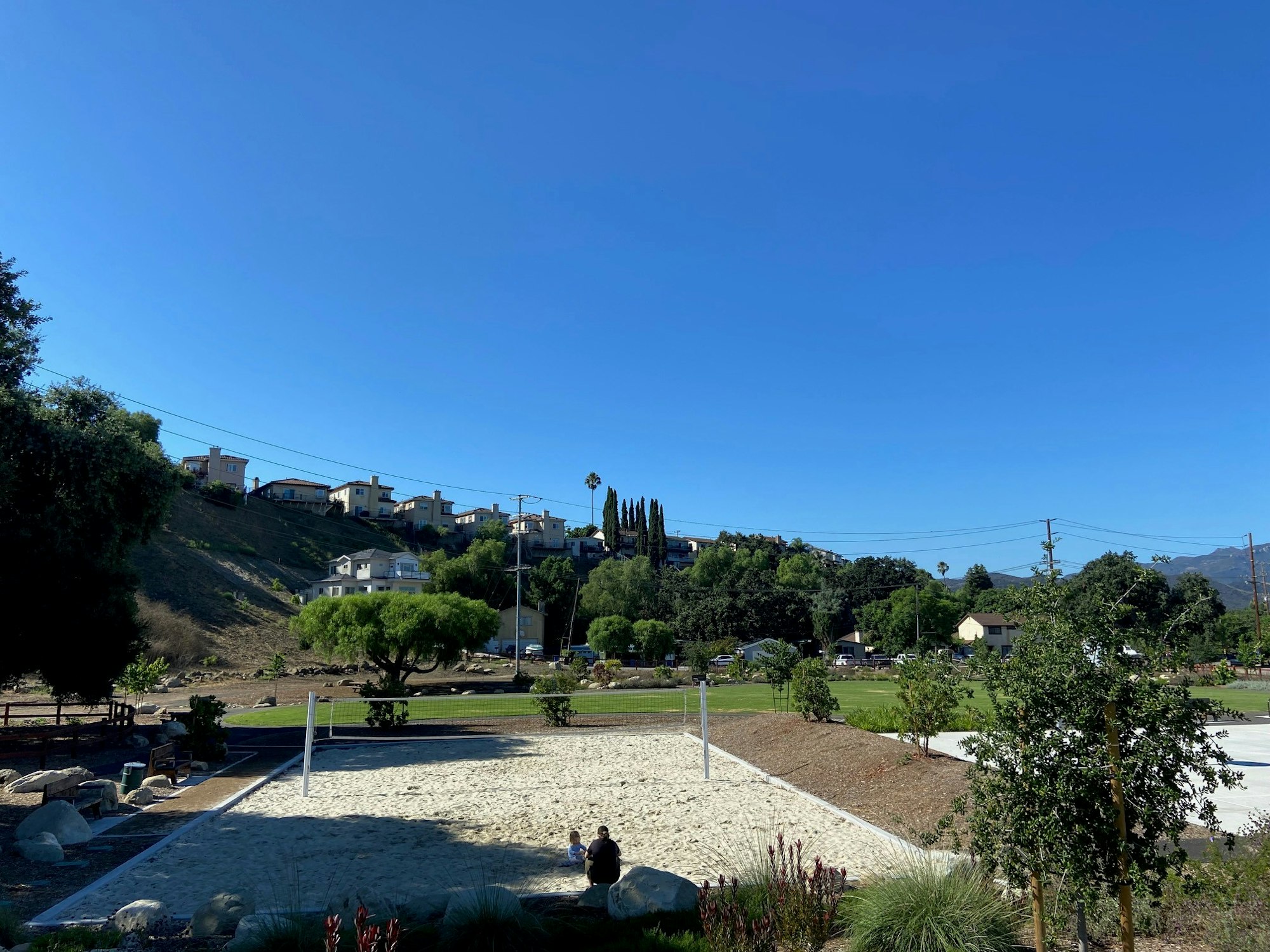 Houses on a hill, volleyball court, and greenery under a clear blue sky.