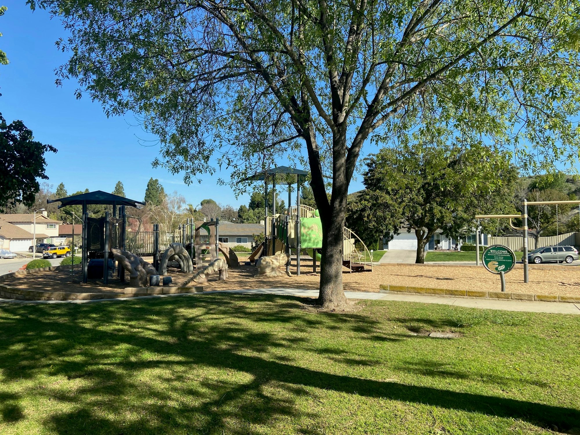 A playground with slides, climbing structures, trees, and grass in a park setting.