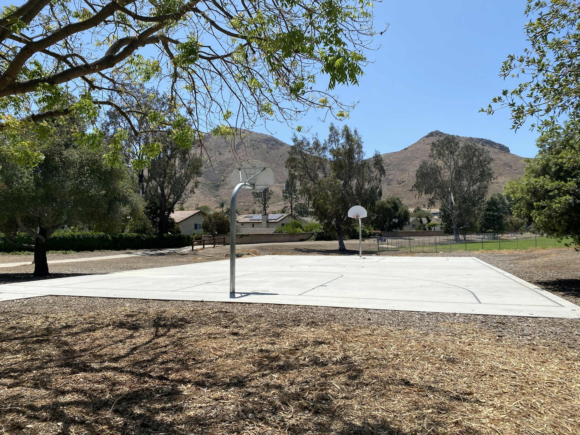 Outdoor basketball court with two hoops, trees, and mountains in the background.