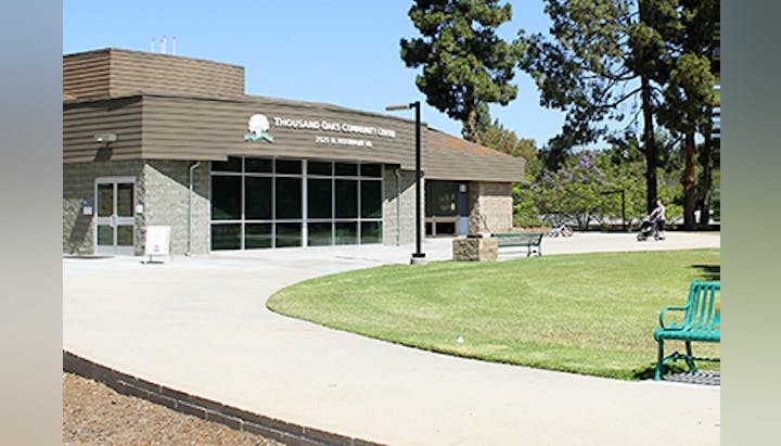 Thousand Oaks Community Center building with a grass area, benches, and trees.