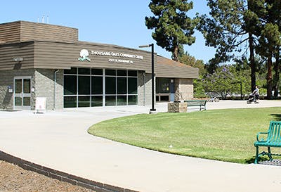 Thousand Oaks Community Center building with a grass area, benches, and trees.