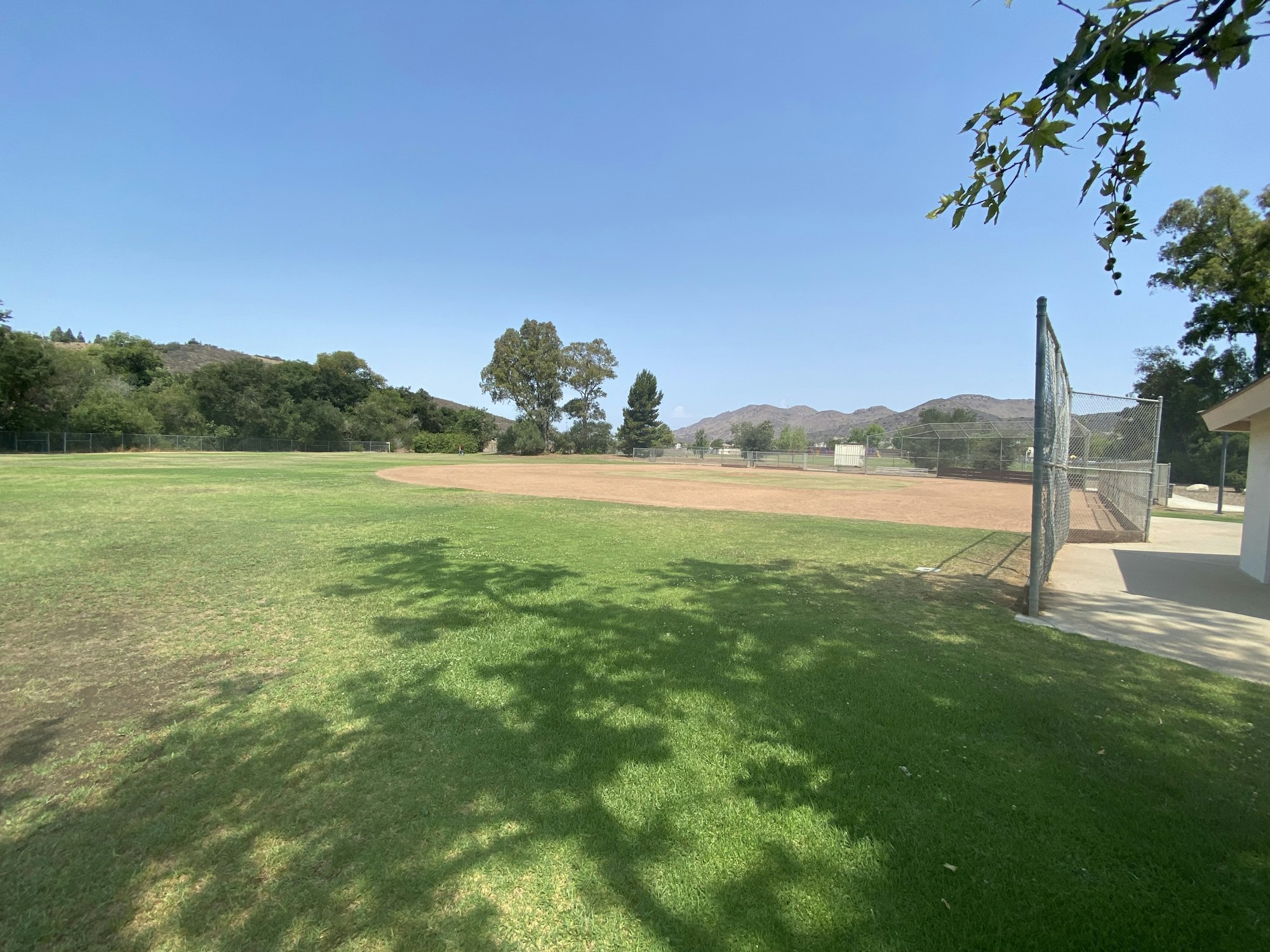 A baseball field under a clear blue sky, surrounded by trees and hills.