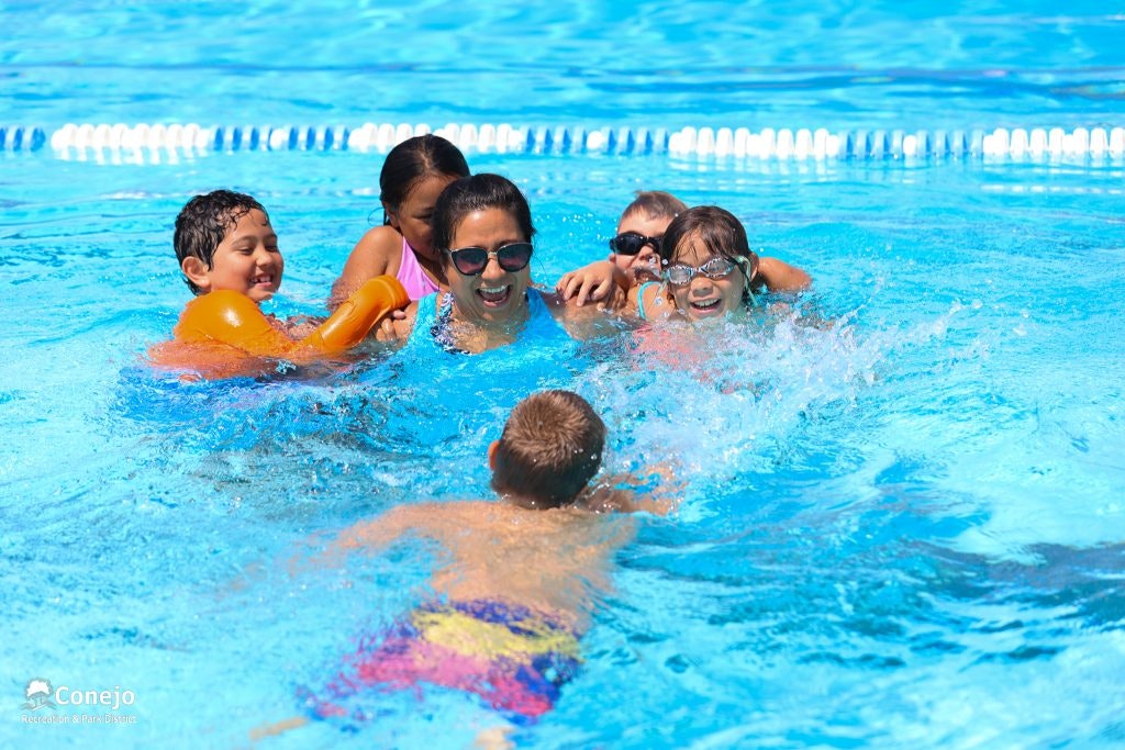 A group of children and an adult enjoying time in a swimming pool.