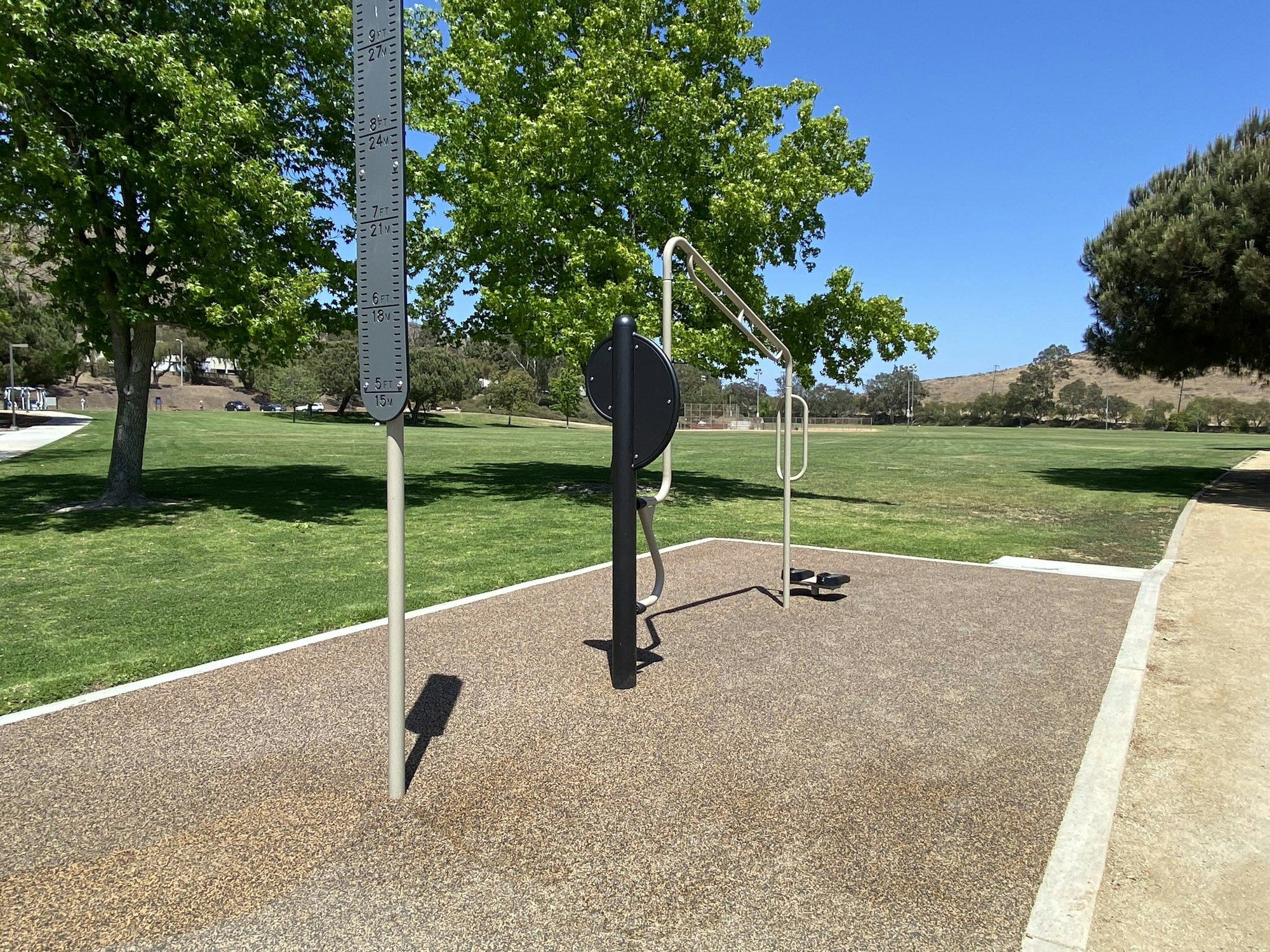 Outdoor fitness equipment in a park with trees and a grassy field.
