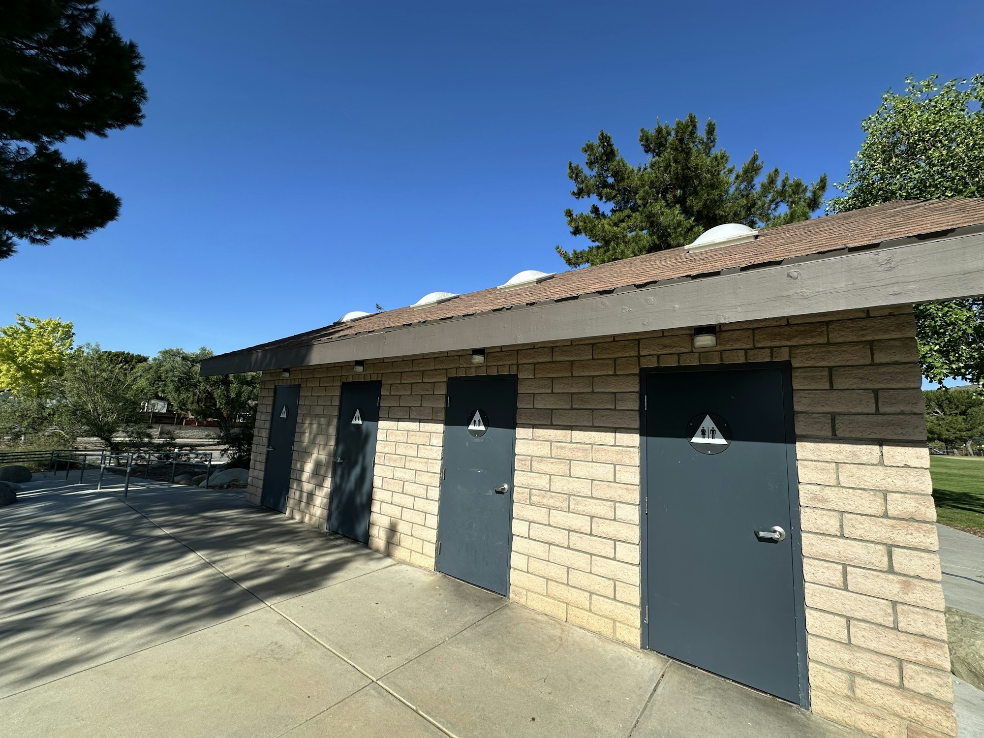 A restroom facility with three doors, set against a clear blue sky and surrounded by trees.