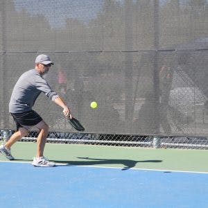 A person playing pickleball, hitting a ball with a paddle on an outdoor court.