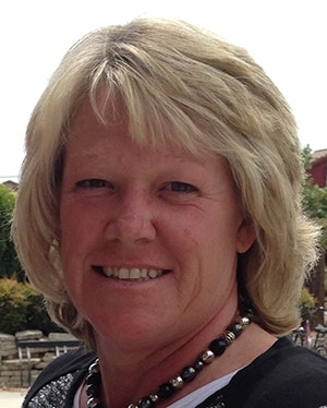 A person with short blonde hair, smiling outdoors.