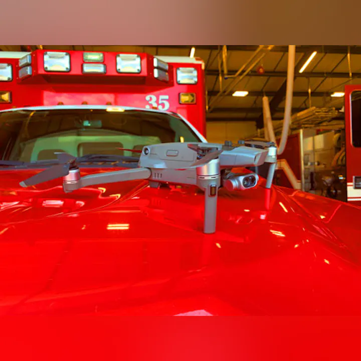 A drone resting on the hood of a red emergency vehicle inside a garage.
