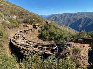 A wooden roller coaster track on a hillside with mountains in the background.