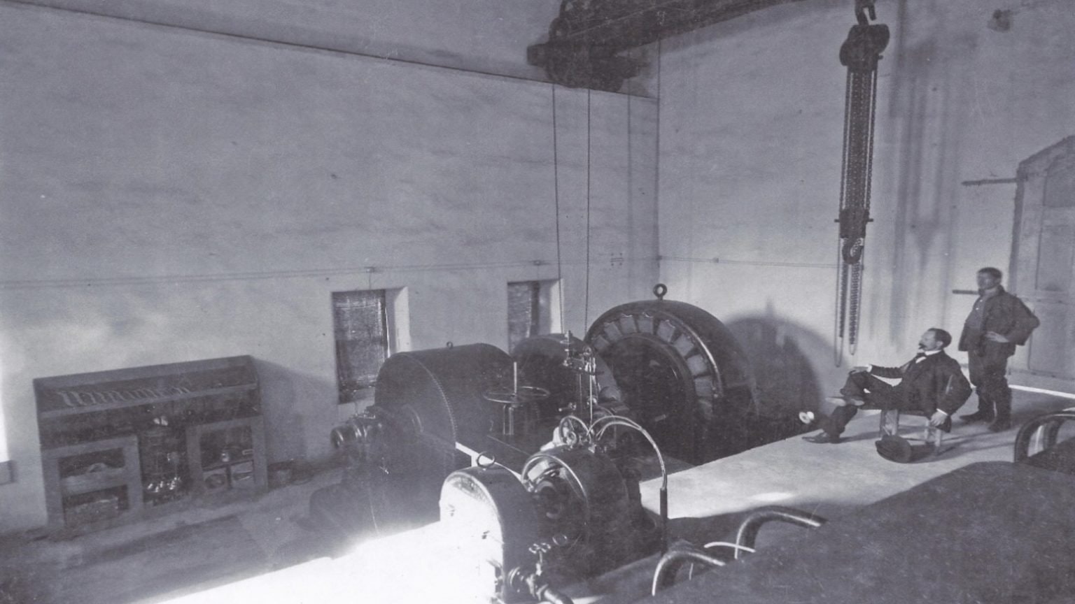 A vintage black-and-white photo of two men in a room with large industrial machinery and equipment.