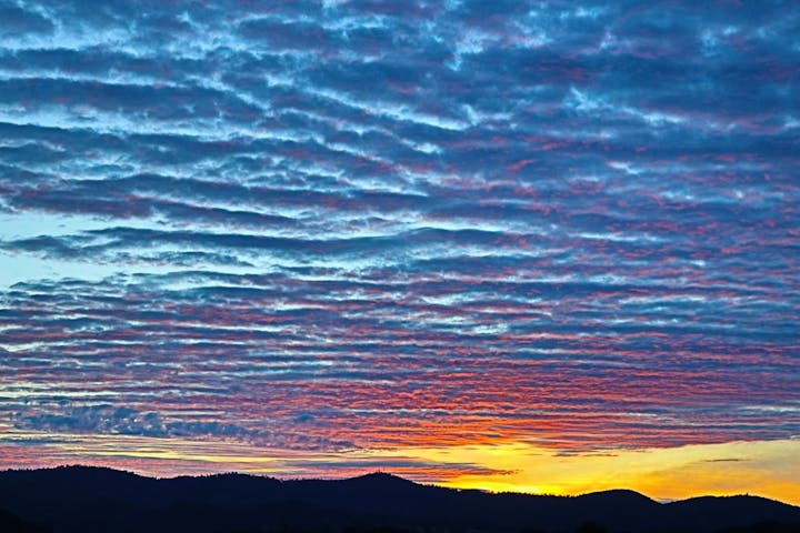 Colorful sunrise with rippled clouds over silhouetted hills.