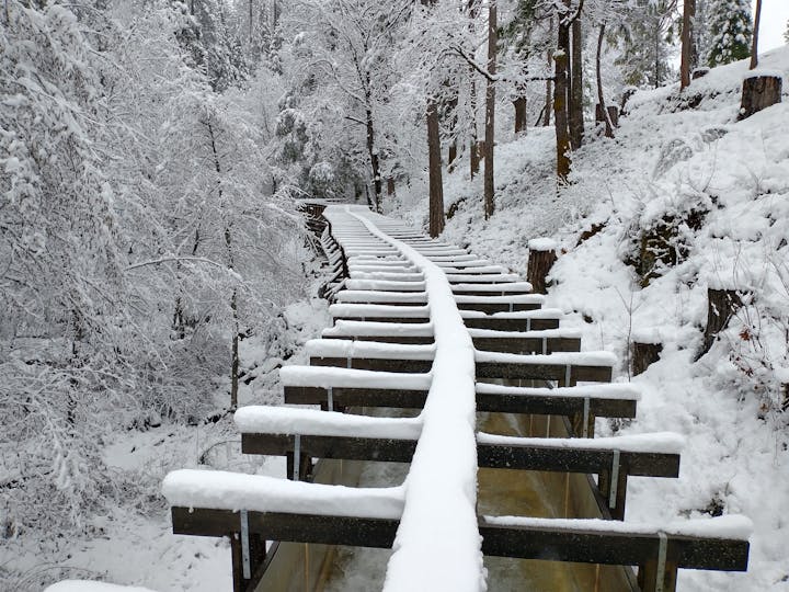 A snow-covered wooden bridge in a forested area, blanketed in snow.