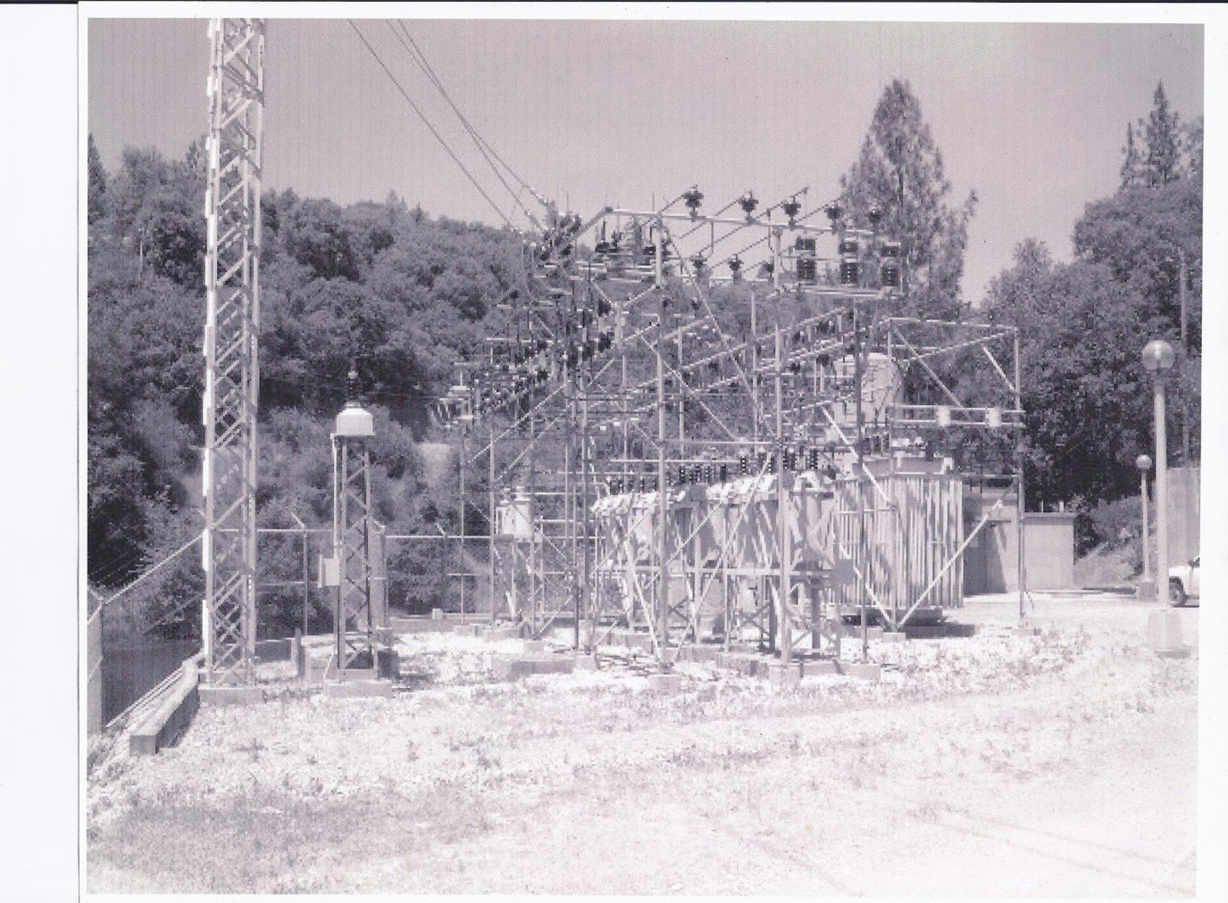 An outdoor electrical substation with towers, transformers, and power lines surrounded by trees.