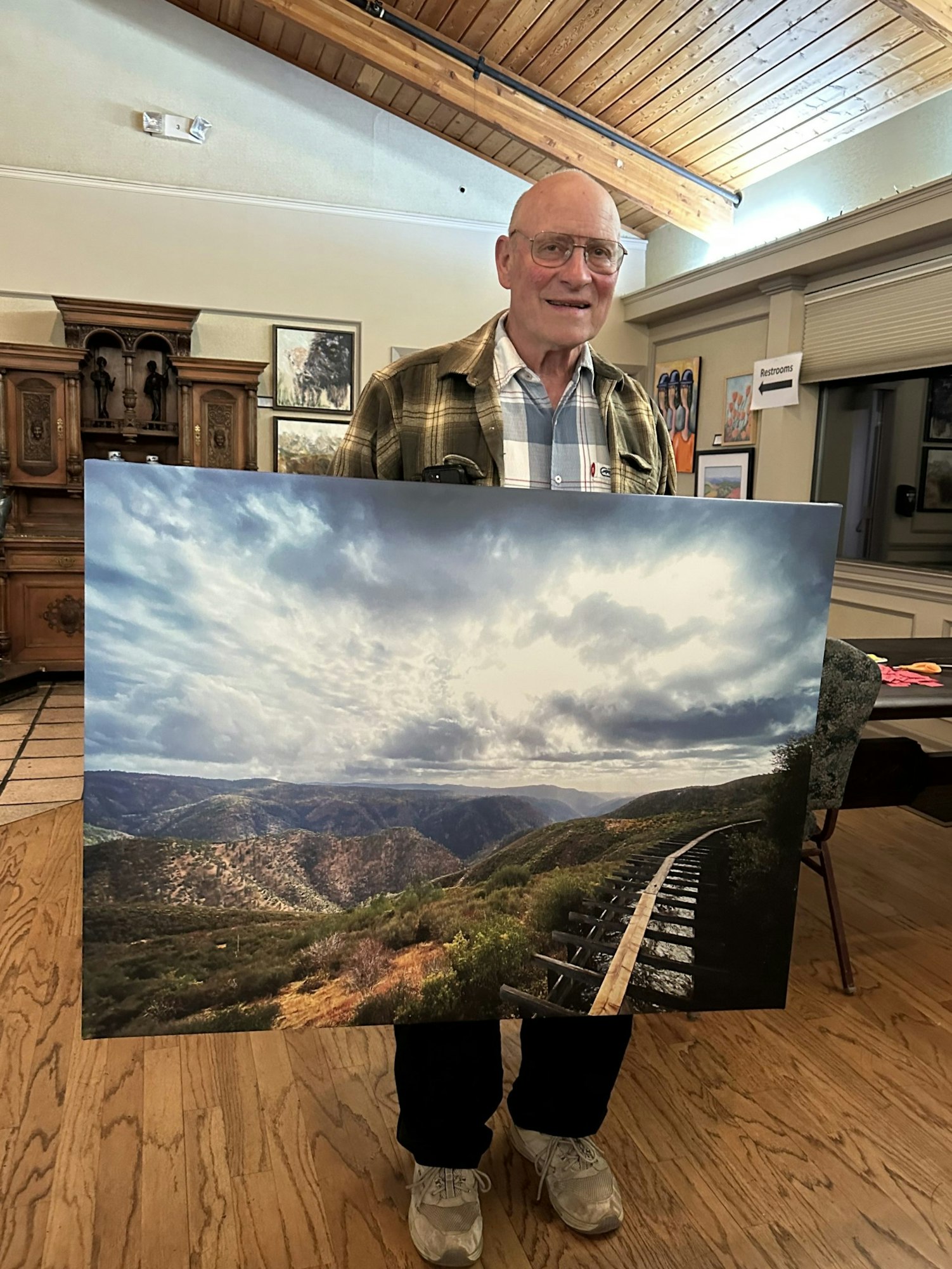 A person holding a large photo of a scenic landscape with mountains and a trail.