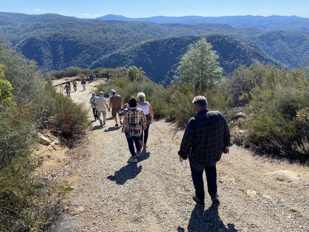 People walking on a trail with mountainous scenery and blue sky.