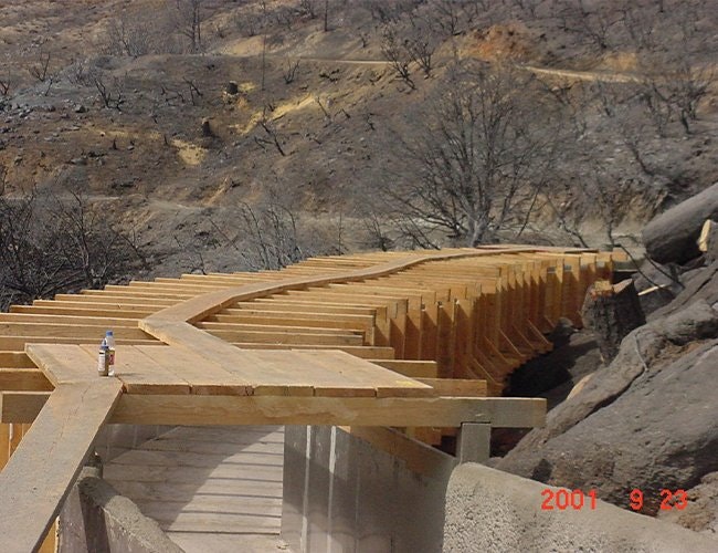 A wooden bridge under construction with a bottle on it, in a dry, barren landscape.