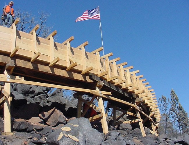 A wooden bridge under construction with an American flag on top, set against a clear blue sky.