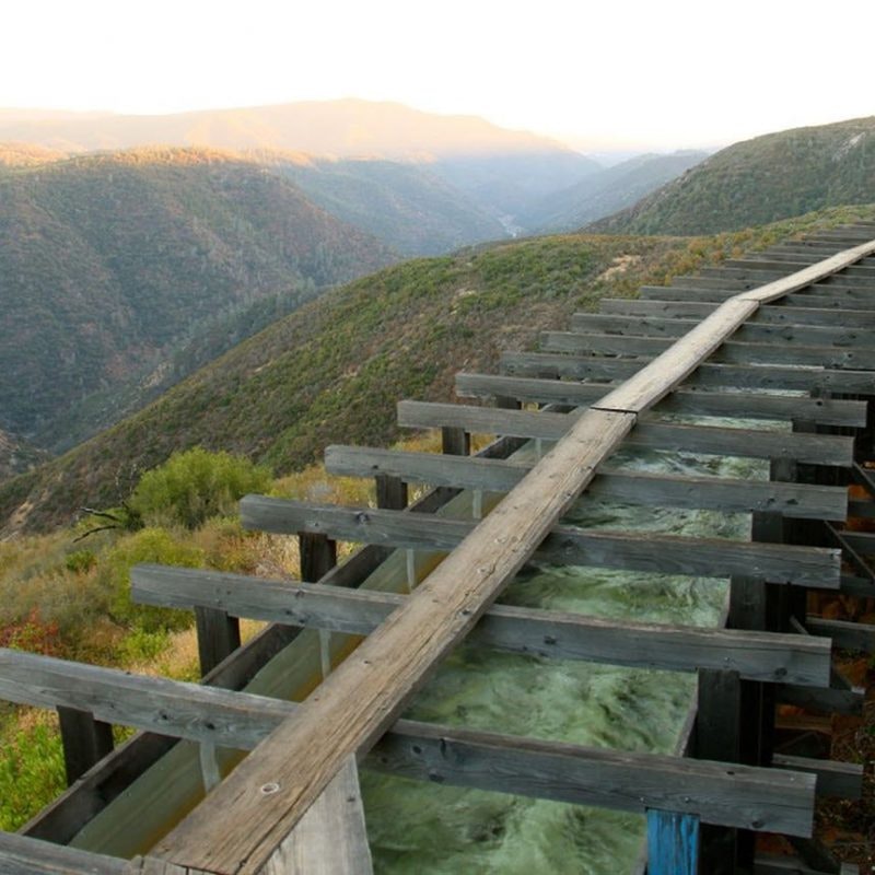 A wooden flume on a hillside, with mountainous landscape in the background.