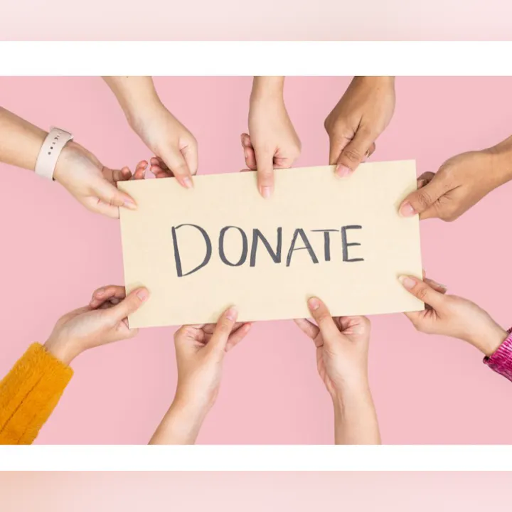 Multiple hands hold up a sign that says "DONATE" against a pink background, promoting charitable giving.