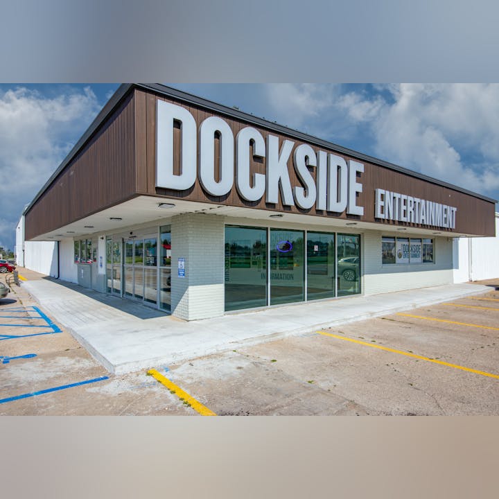 A building with "Dockside Entertainment" signage, featuring large glass windows and accessible entry, in a parking lot.