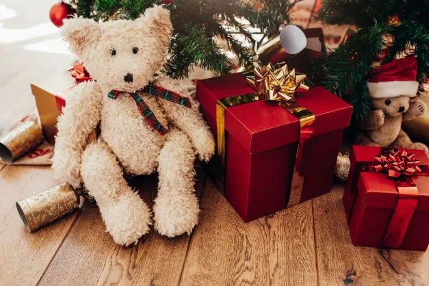 A teddy bear with Christmas gifts under a festive tree.