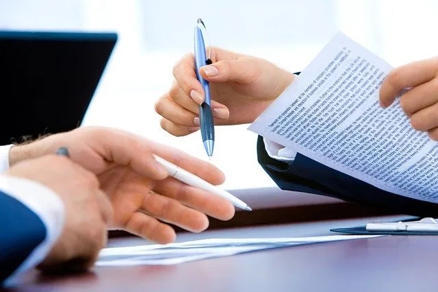 Two individuals reviewing a document, one holding a pen, likely in a business setting.