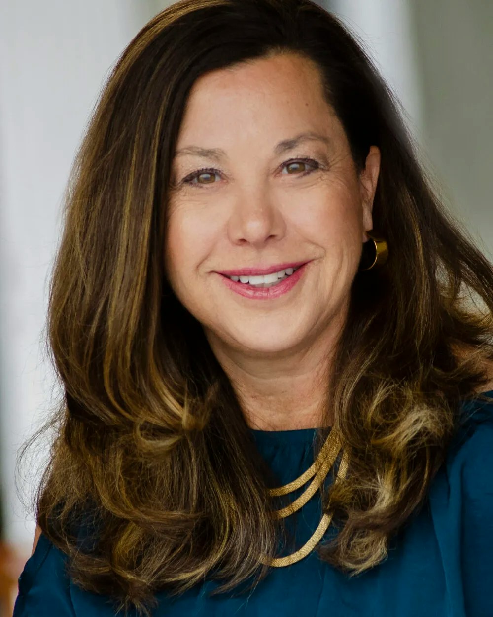 A smiling woman with long hair, gold earrings, and necklace.