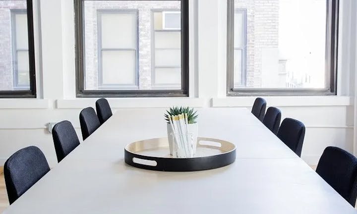 A minimalist conference room with a white table, chairs, and a tray with a plant on the table.