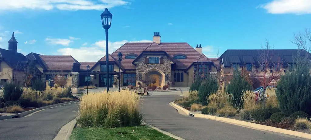 A street leading to a grand building with a tiled roof, surrounded by ornamental grasses under a blue sky.