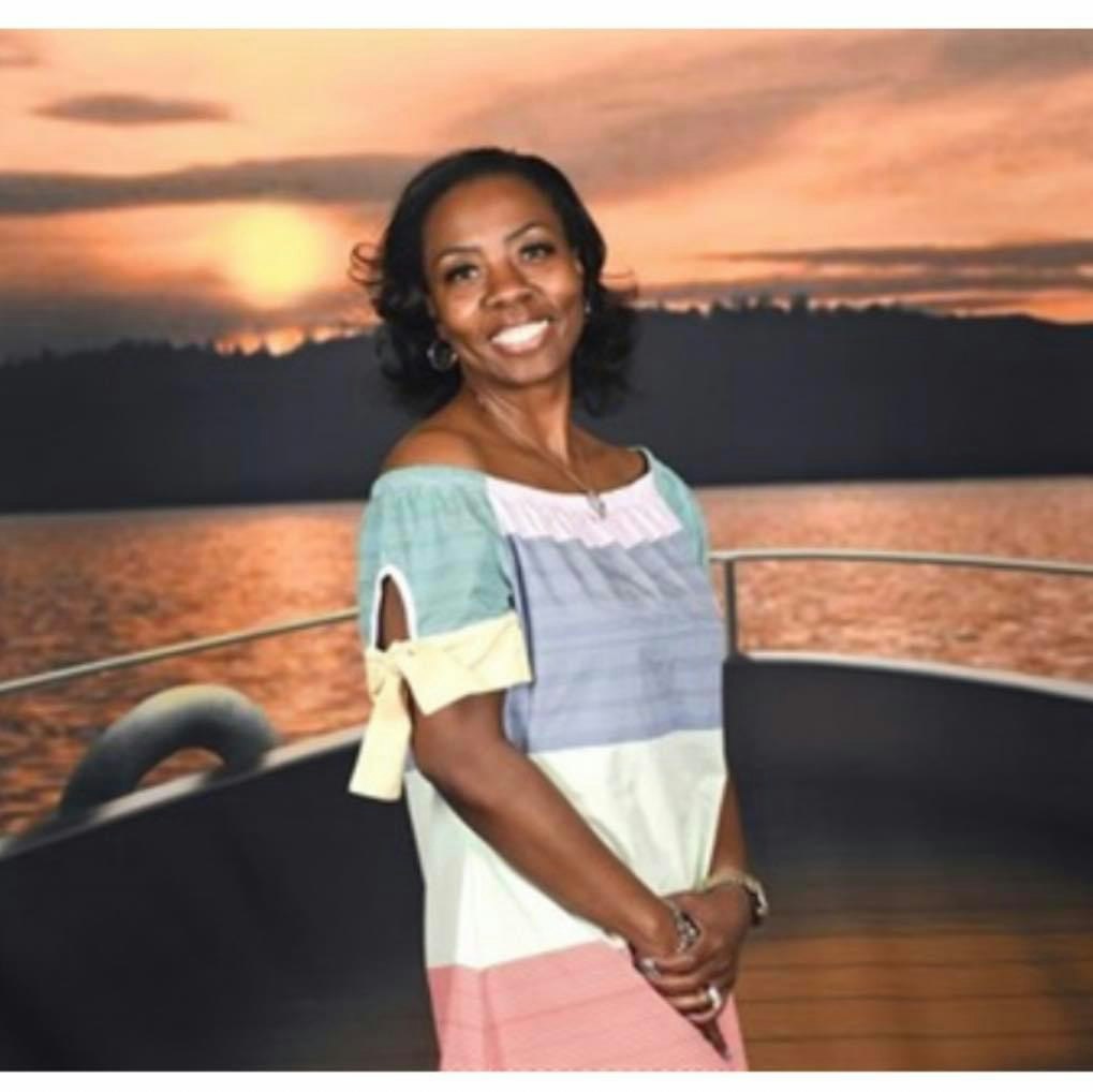 A person smiling on a boat deck with a sunset over the water in the background.