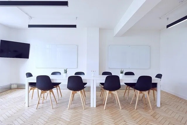 Modern meeting room with table, chairs, whiteboards, and TV.