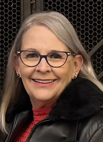 A person with glasses, smiling, wearing a jacket with a fur collar.