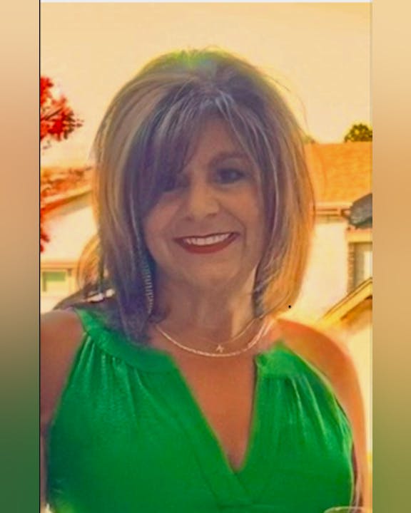 A person smiling, wearing a green top, with a house and trees in the background.