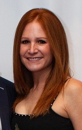 A person with long red hair smiling, wearing a black top.