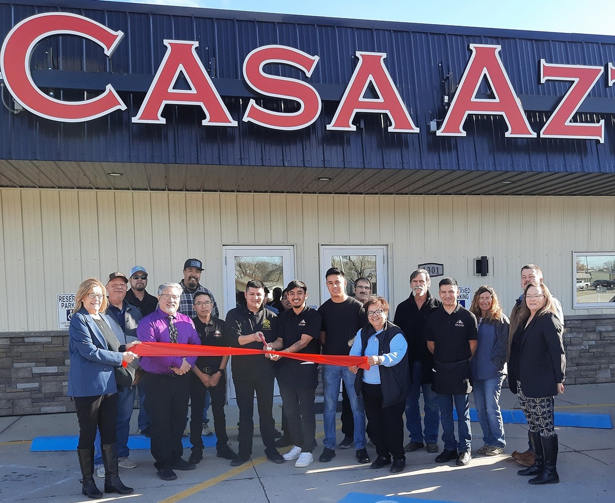 A group of people holding a red ribbon in front of a building with the sign "CASA AZT."