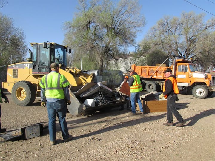 Workers with a wheel loader and dump truck moving debris.