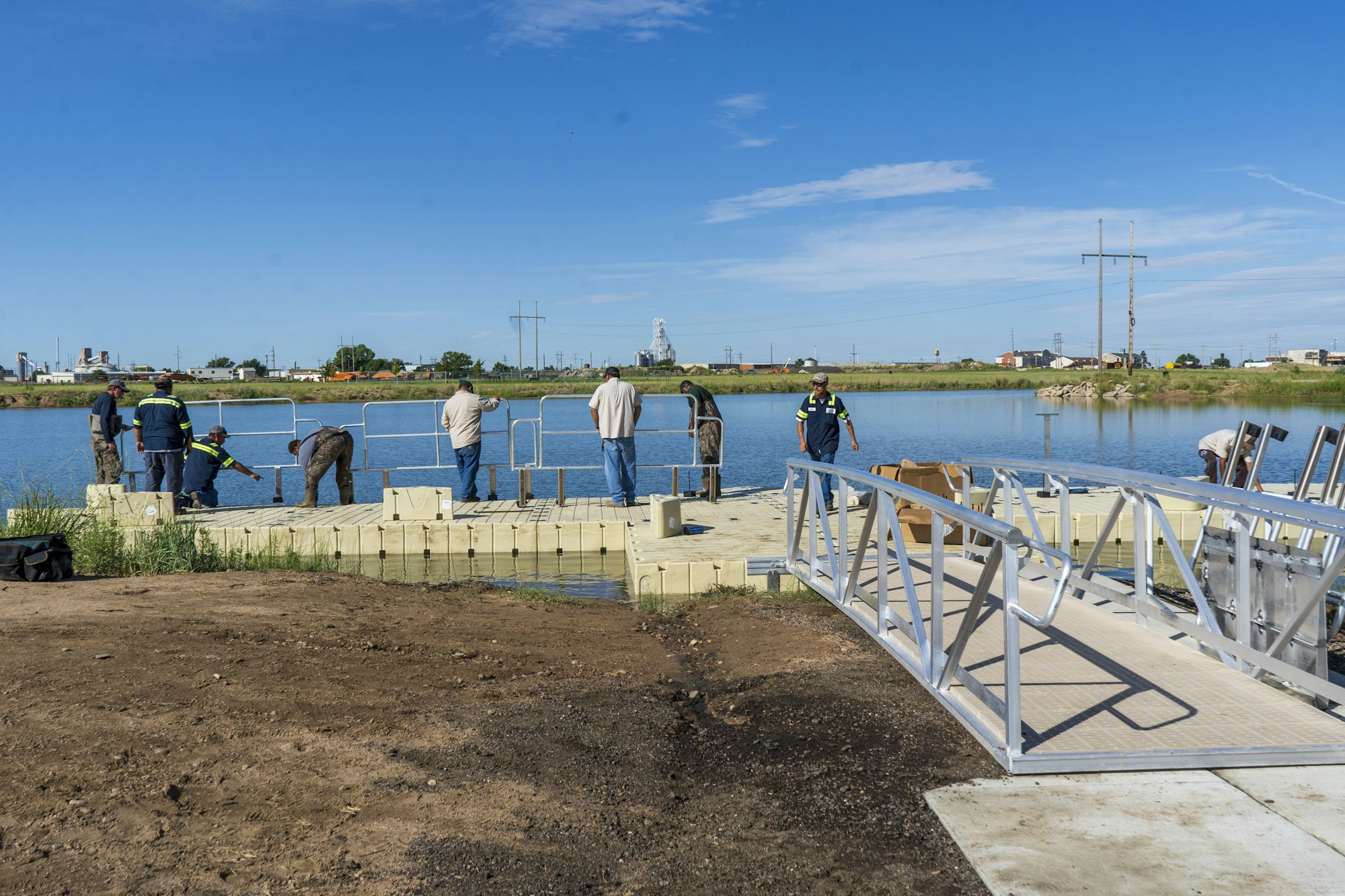 People assembling a dock on a lakeshore under a clear blue sky.