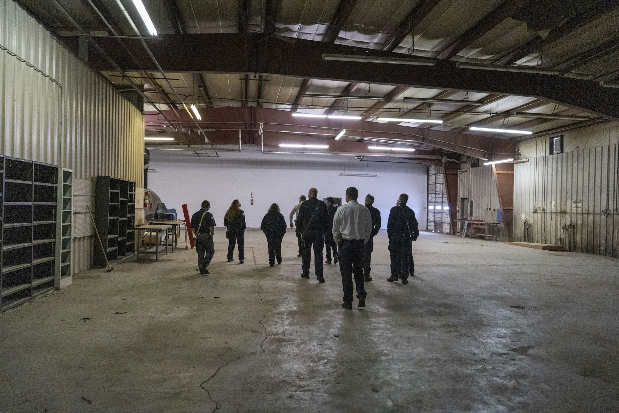 Group of people walking in an industrial warehouse with high ceilings and shelves.