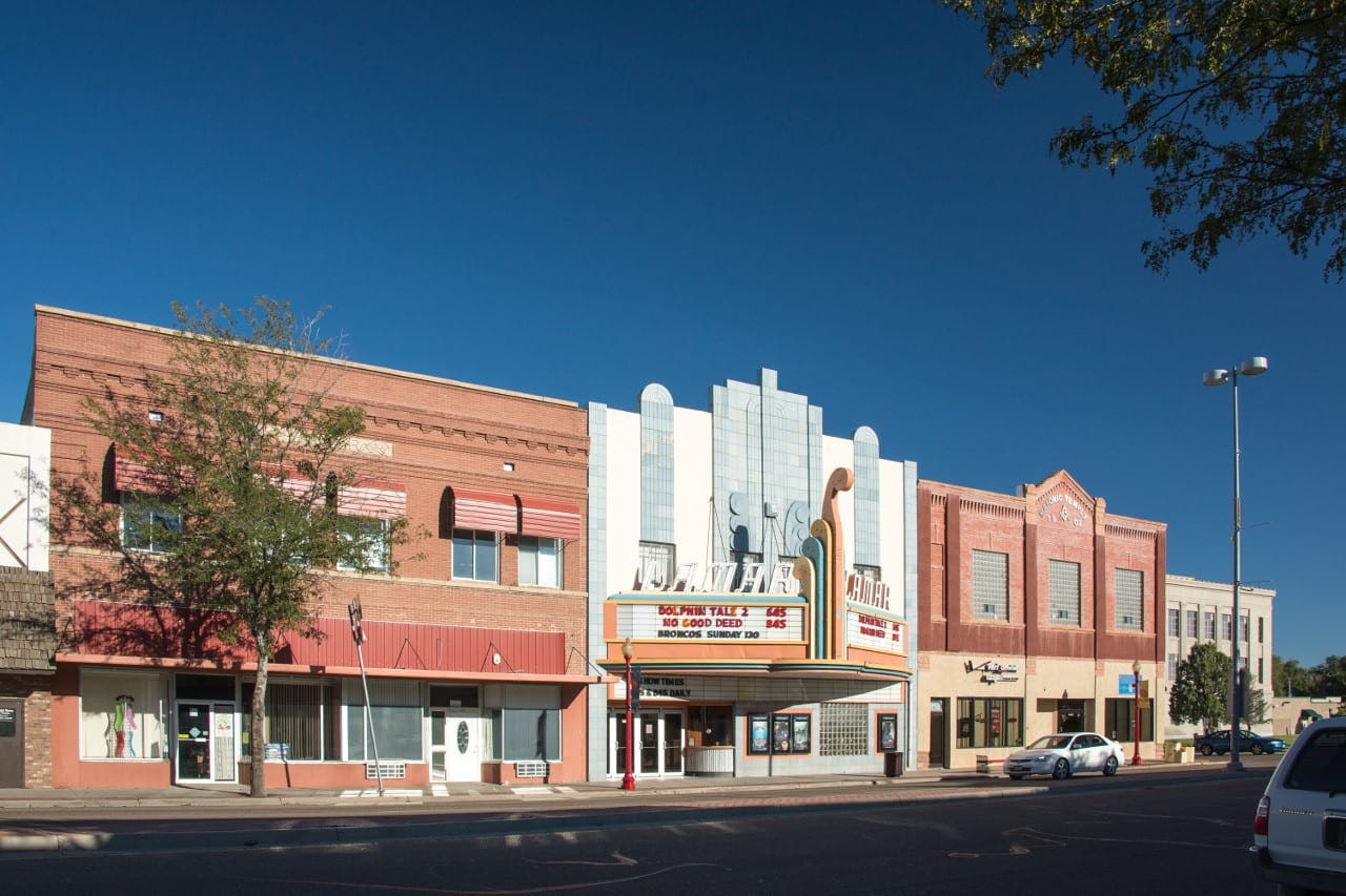 A sunny street view featuring an Art Deco-style movie theater marquee and adjacent buildings.