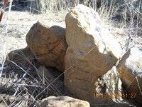 A pile of large rocks surrounded by dry grass and sunlight.