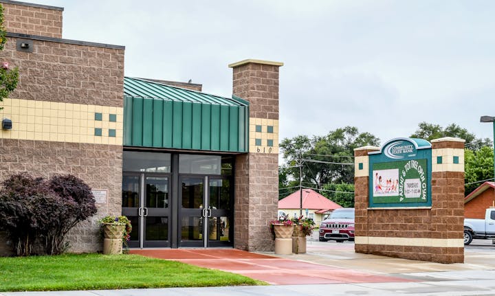 Building entrance with green roof, brick walls, sign for Community State Bank, and plants.