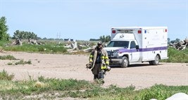 A firefighter walking near an ambulance with debris in the background.